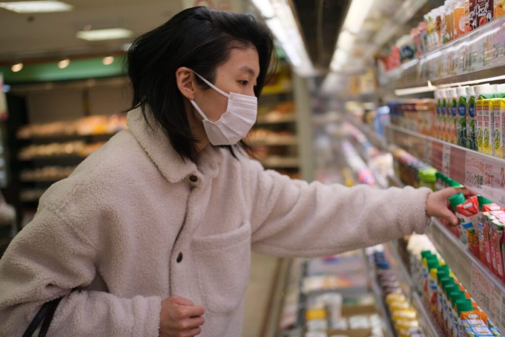 A imagem é a fotografia de uma mulher asiática de pele branca escolhendo um produto em uma prateleira em um mercado. A imagem ilustra a recuperação tributária para supermercados, o tema deste artigo.