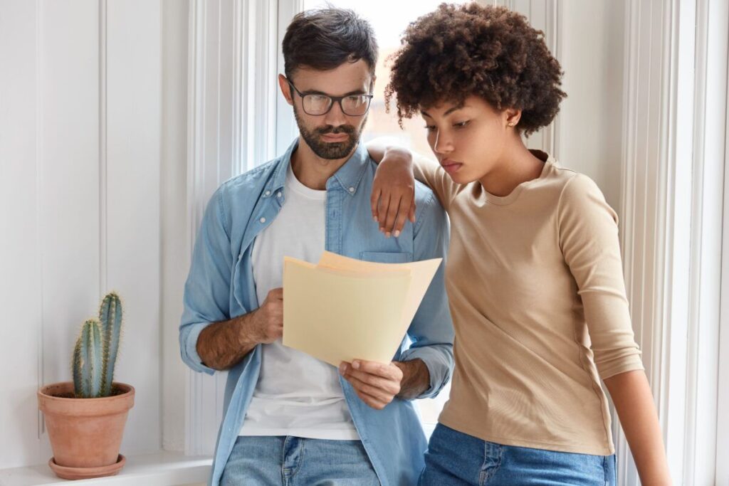 A imagem é a fotografia em cores de um casal heterossexual analisando juntos um documento. O documento está na mão do homem, que tem a pela branca, barba e cabelos pretos e usa barba, enquanto a mulher, que tem um cabelo crespo e a pele negra,  está apoiada em seus ombros. A fotografia leva a entender que o casal são inquilinos. A imagem ilustra a recuperação tributária  para condomínios.