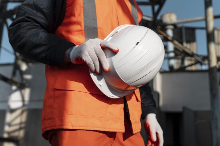 A imagem se trata de uma fotografia de um homem da construção civil vestido com um uniforme laranja segurando um capacete de obras na cor branca. A foto representa a tributação para construção civil, o tema deste artigo.