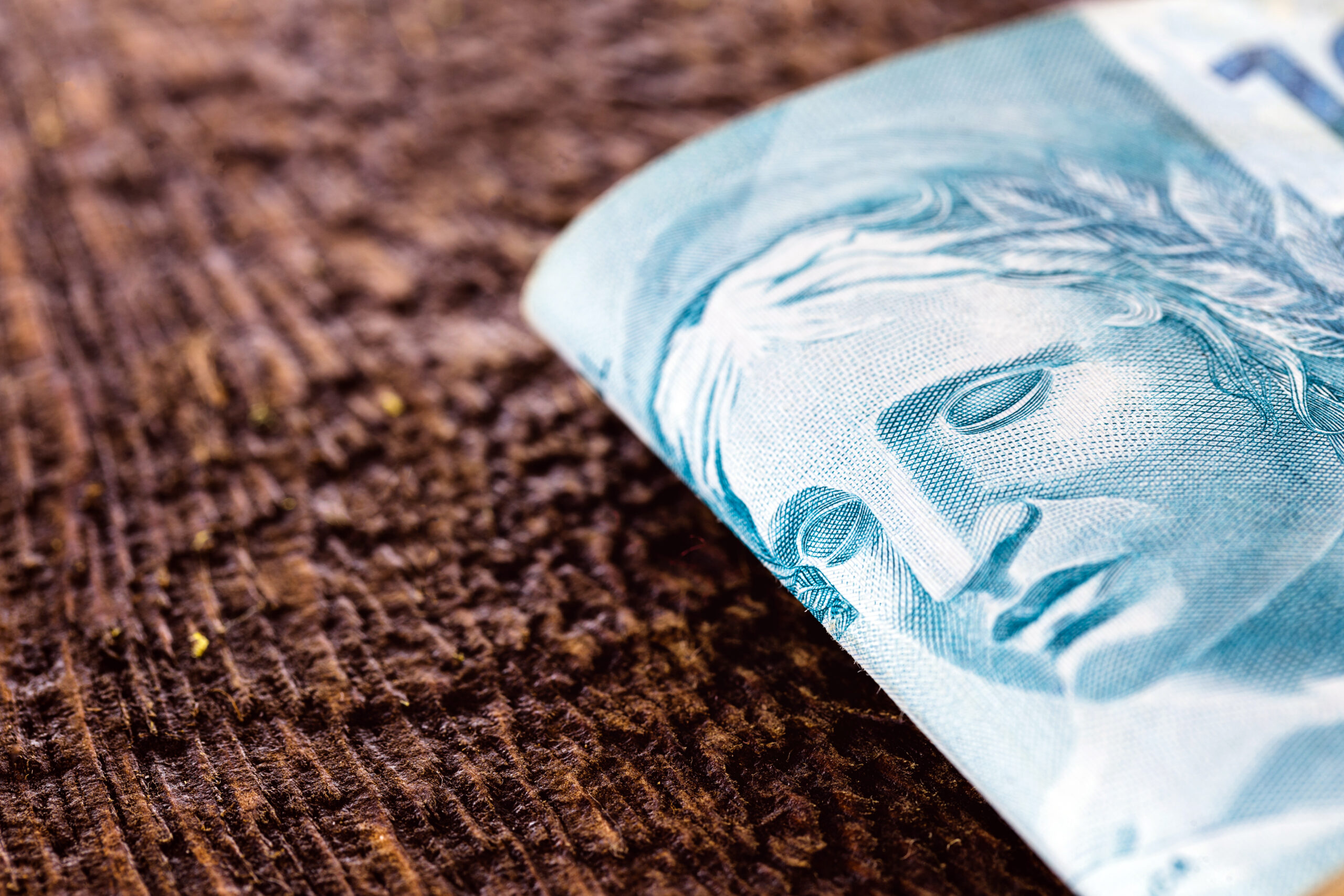 Detalhe de uma nota de cem reais sobre superfície de madeira, simbolizando gestão financeira, carga tributária e decisões sobre o regime do Simples Nacional.